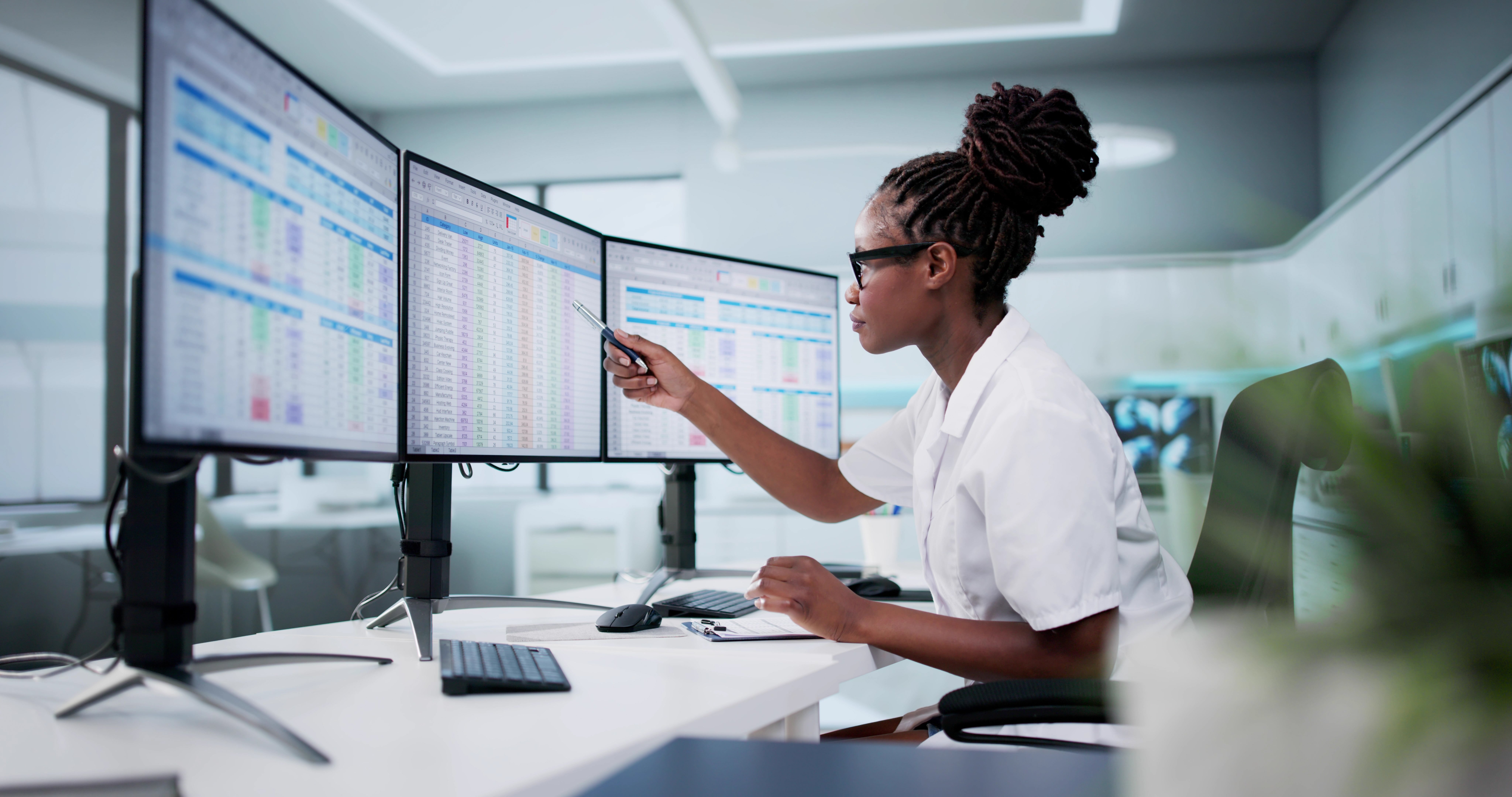 Healthcare professional reviewing electronic records and documentation across multiple computer monitors.